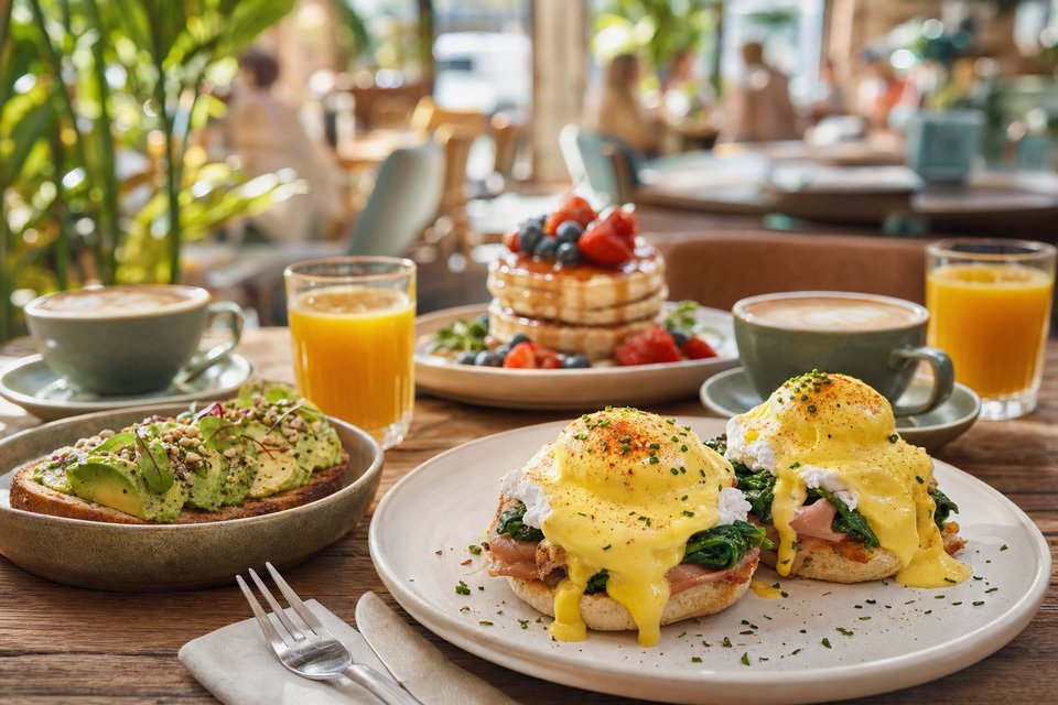 Brunchtafel met eggs benedict, pannenkoeken met bessen, avocadotoast, cappuccino en jus d'orange in de ochtendzon (met AI gemaakte afbeelding)